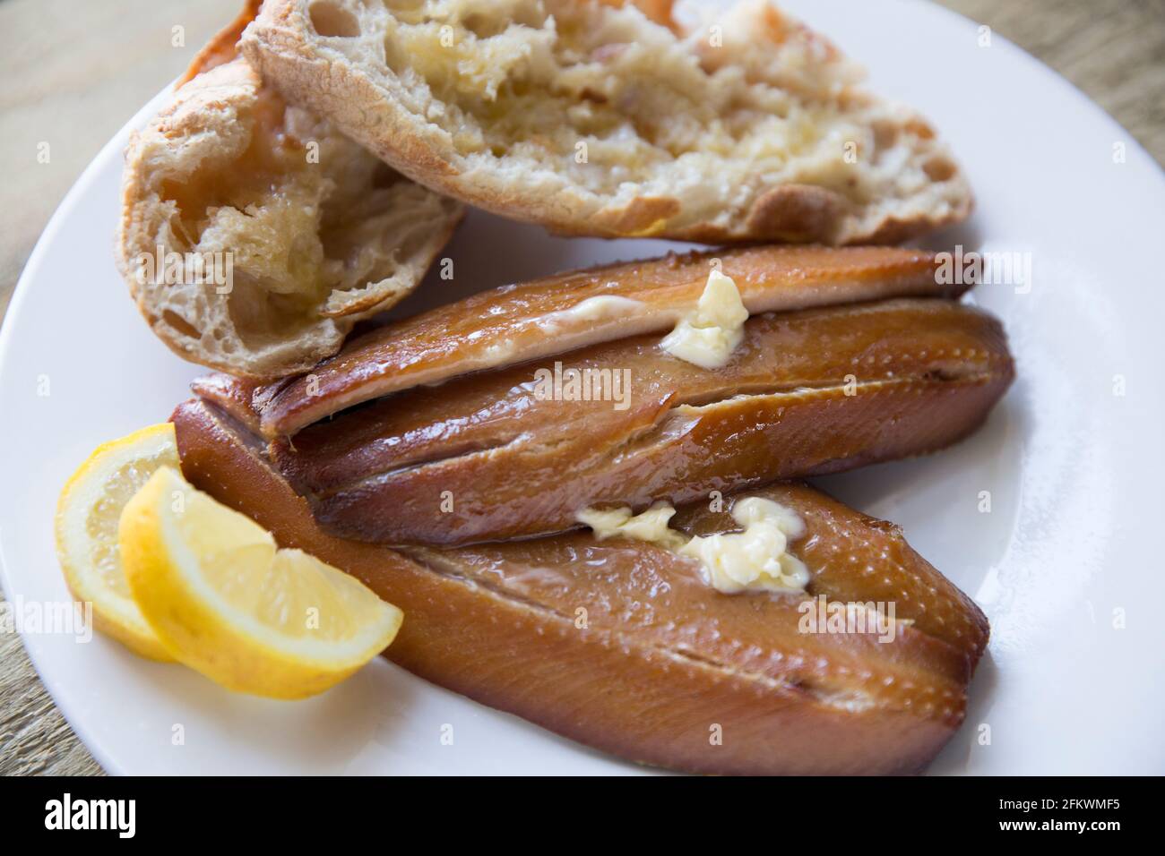 Smoked Craster kipper cutlets presented on a wooden background. Kippers are smoked herrings and are rich in fish oils. Served with warm bread, butter Stock Photo