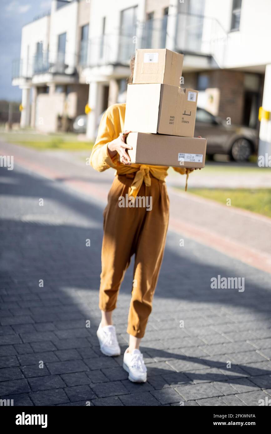 Woman holding parcels on the street in front of the house. Received the ordered goods at the post office. Online shopping. Delivery service.  Stock Photo