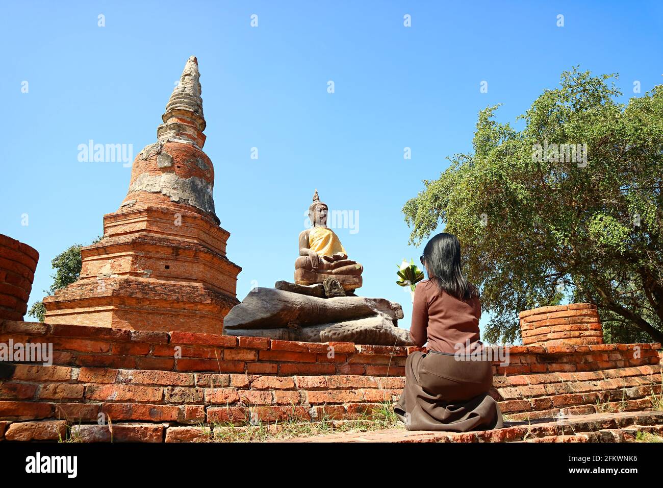 Woman praying in front of Buddha image at Wat Phra Ngam temple ruins in Ayutthaya, Thailand Stock Photo