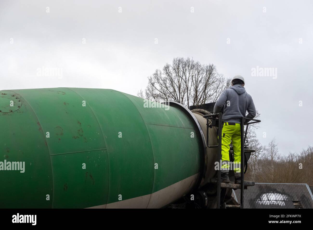 Man worker on a ladder checking concrete mixer truck. Construction worker in housing development. Stock Photo