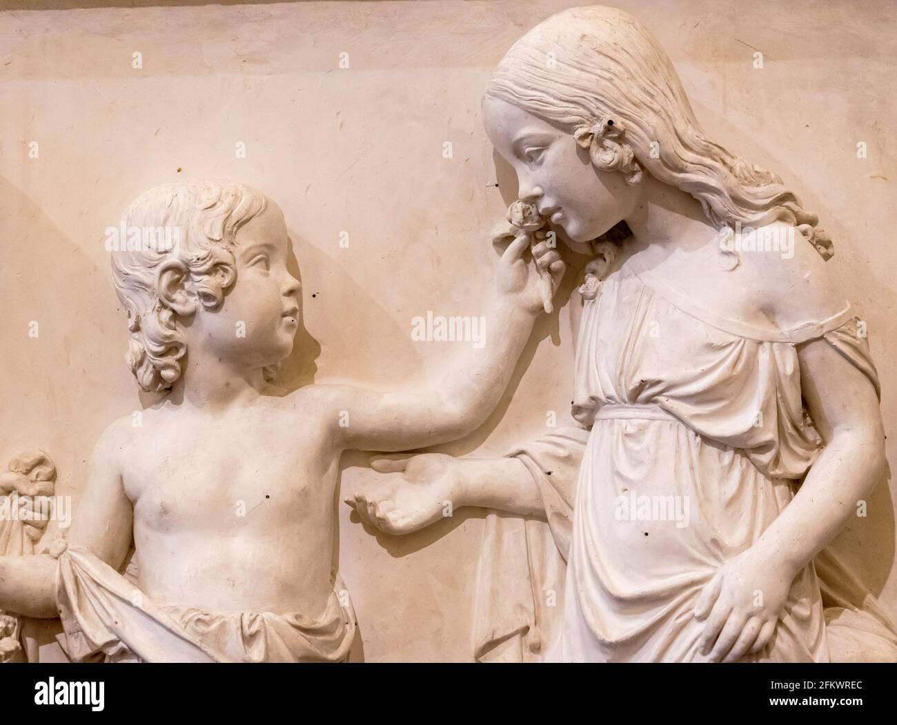 Close-up on sculptures carved on marble wall showing a girl smelling a flower given by a boy Stock Photo