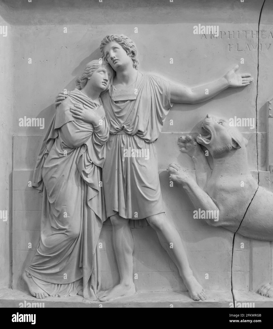 Black and white photo of sculptures carved on marble wall showing a couple holding each other while attacked by a lioness Stock Photo