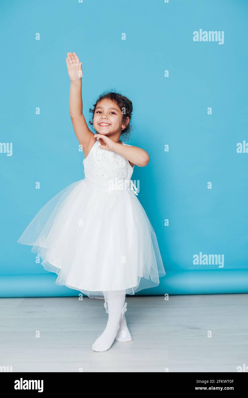 Beautiful little girl dances to the song in a white dress on a blue