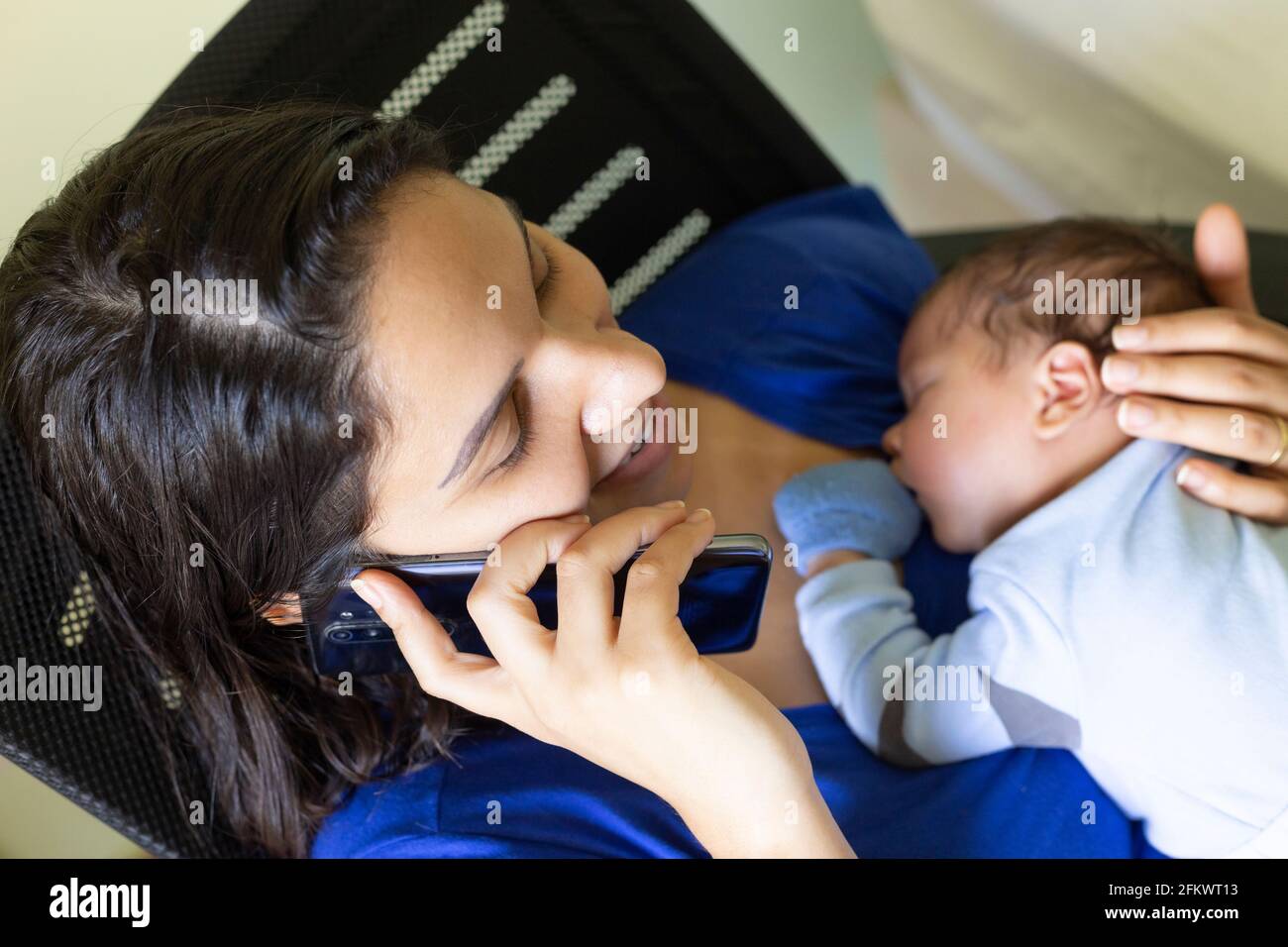 Happy woman talking on the phone with baby on her lap. Stock Photo