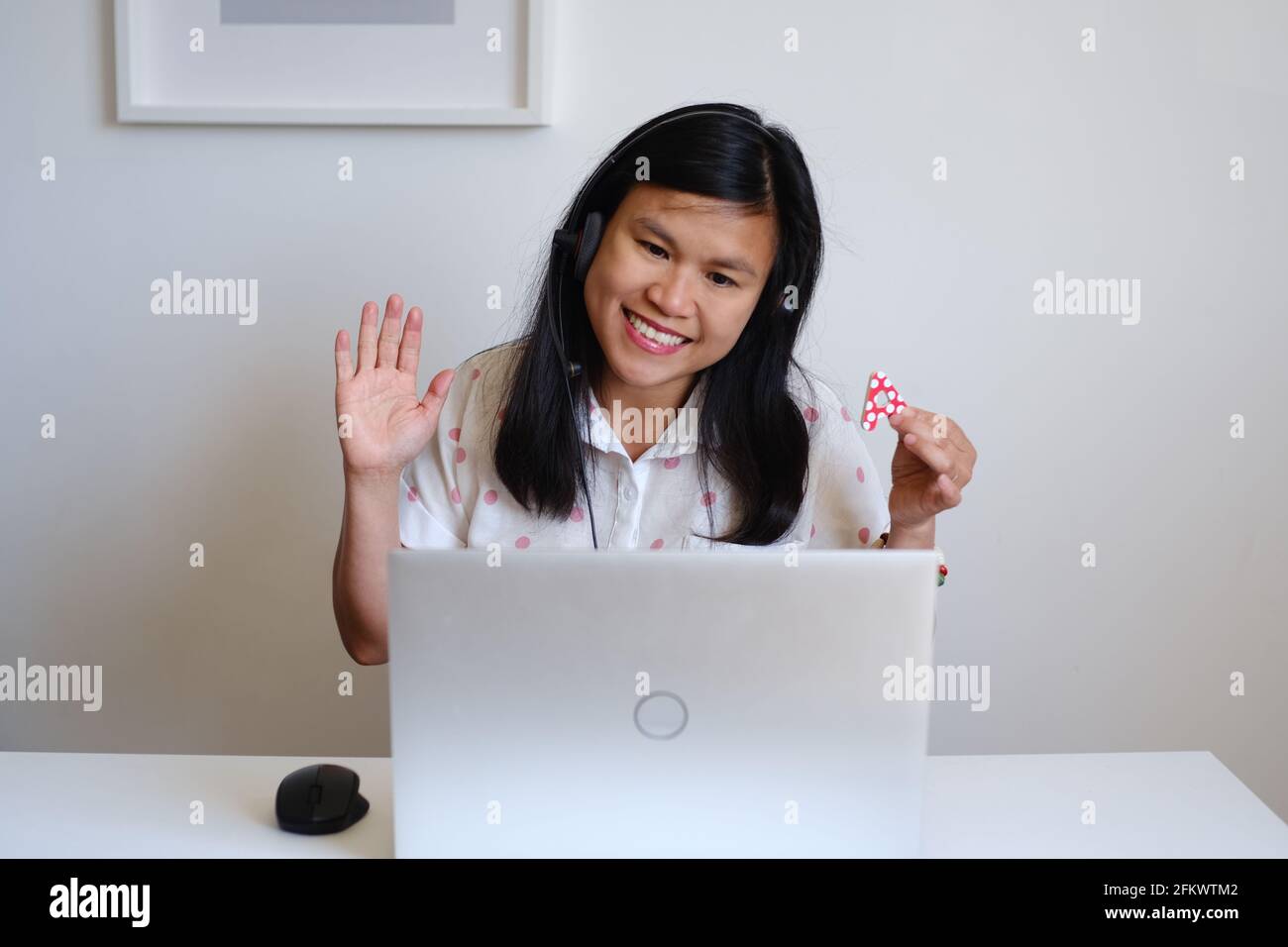 Filipino filipina Asian woman or girl teacher working sitting in front of a white desk and silver computer, teaching a lesson online on the Internet Stock Photo