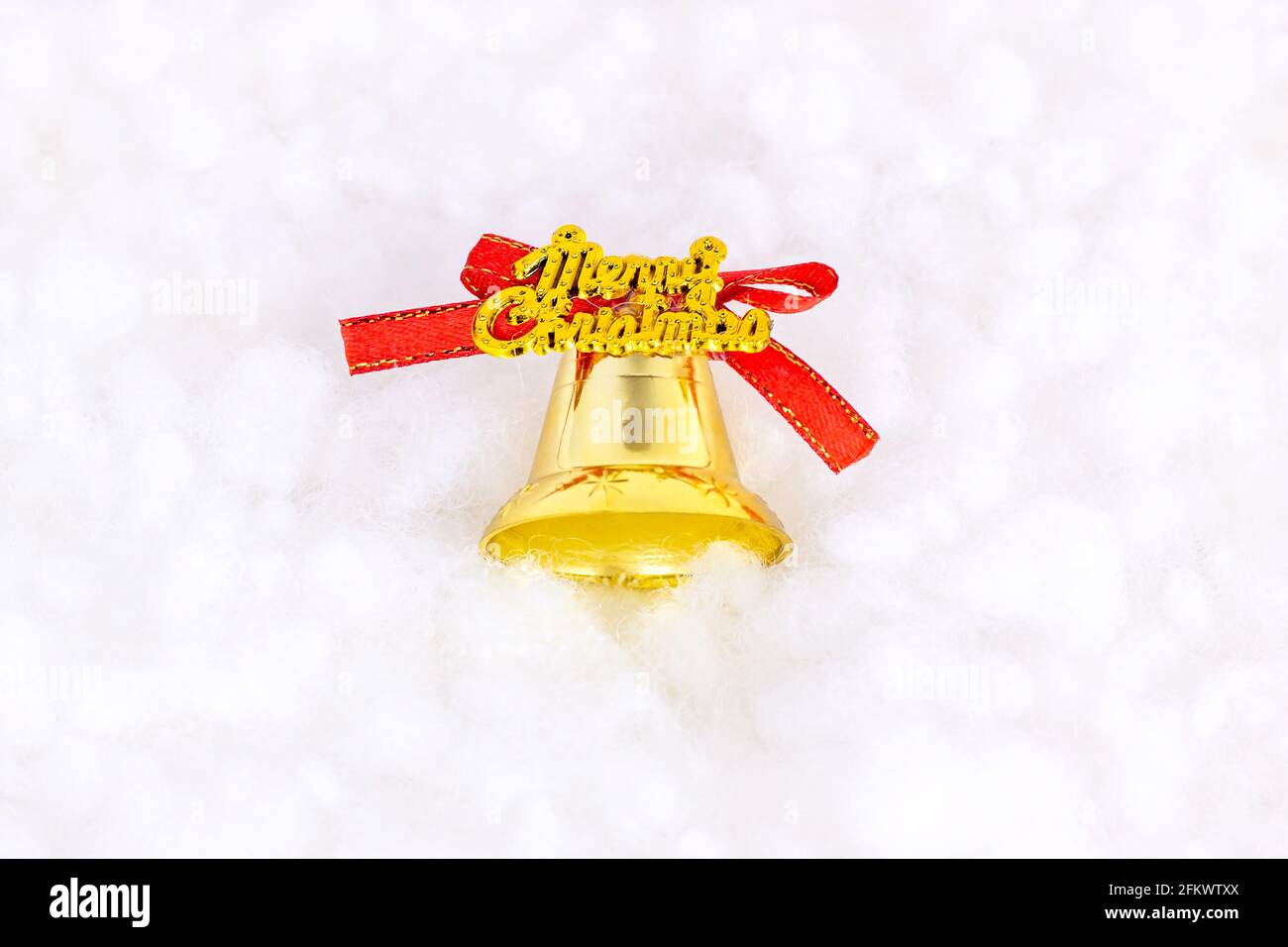 Bright golden Christmas decoration bell on white artificial snow background with copy space. Christmas and New Year traditional holiday celebration co Stock Photo