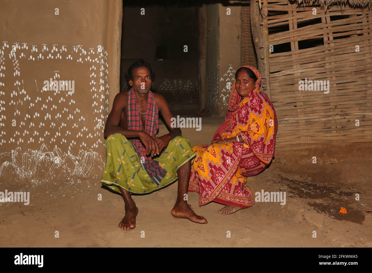 Tribal couple sitting at the entrance of their house . Traditional decorated Chita painting is also seen in the picture .KOLI TRIBE. Odasinga Jodum Stock Photo