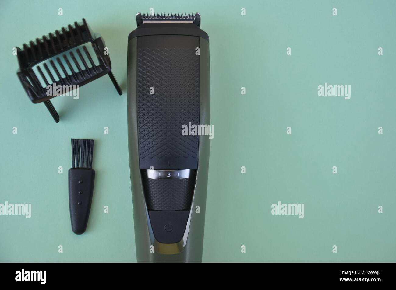 High angle shot of beard trimmer with comb and brush with negative space, Hair trimmer isolated on green background. Stock Photo