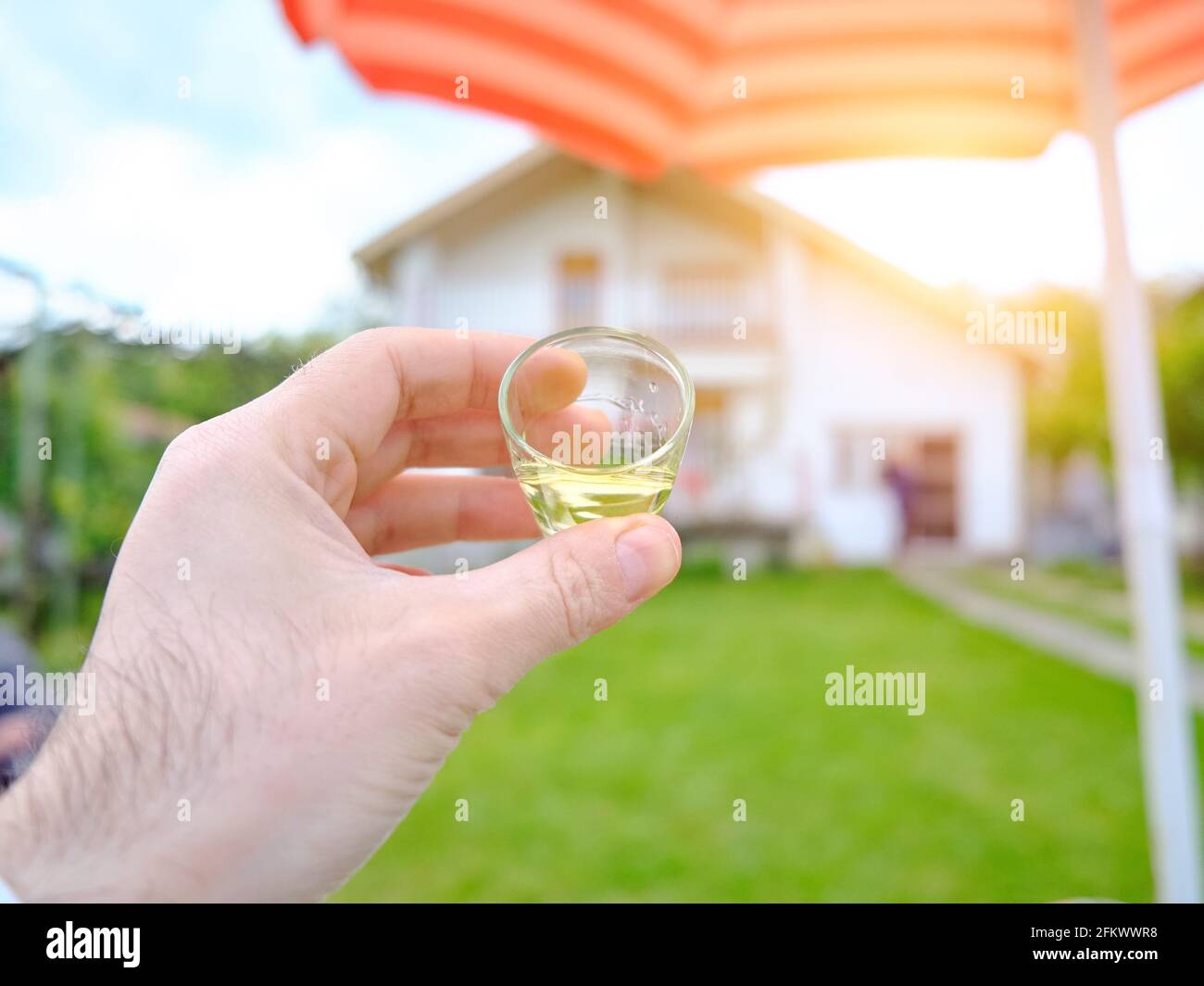 POV of drinking alcoholic drink from a small glass in home yard Stock Photo