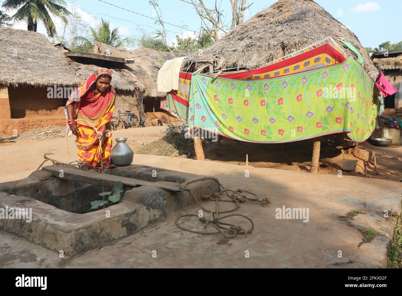 Woman drawing water from a well with rope and container at Kuanarpal village of Cuttack district of Odisha, India Stock Photo