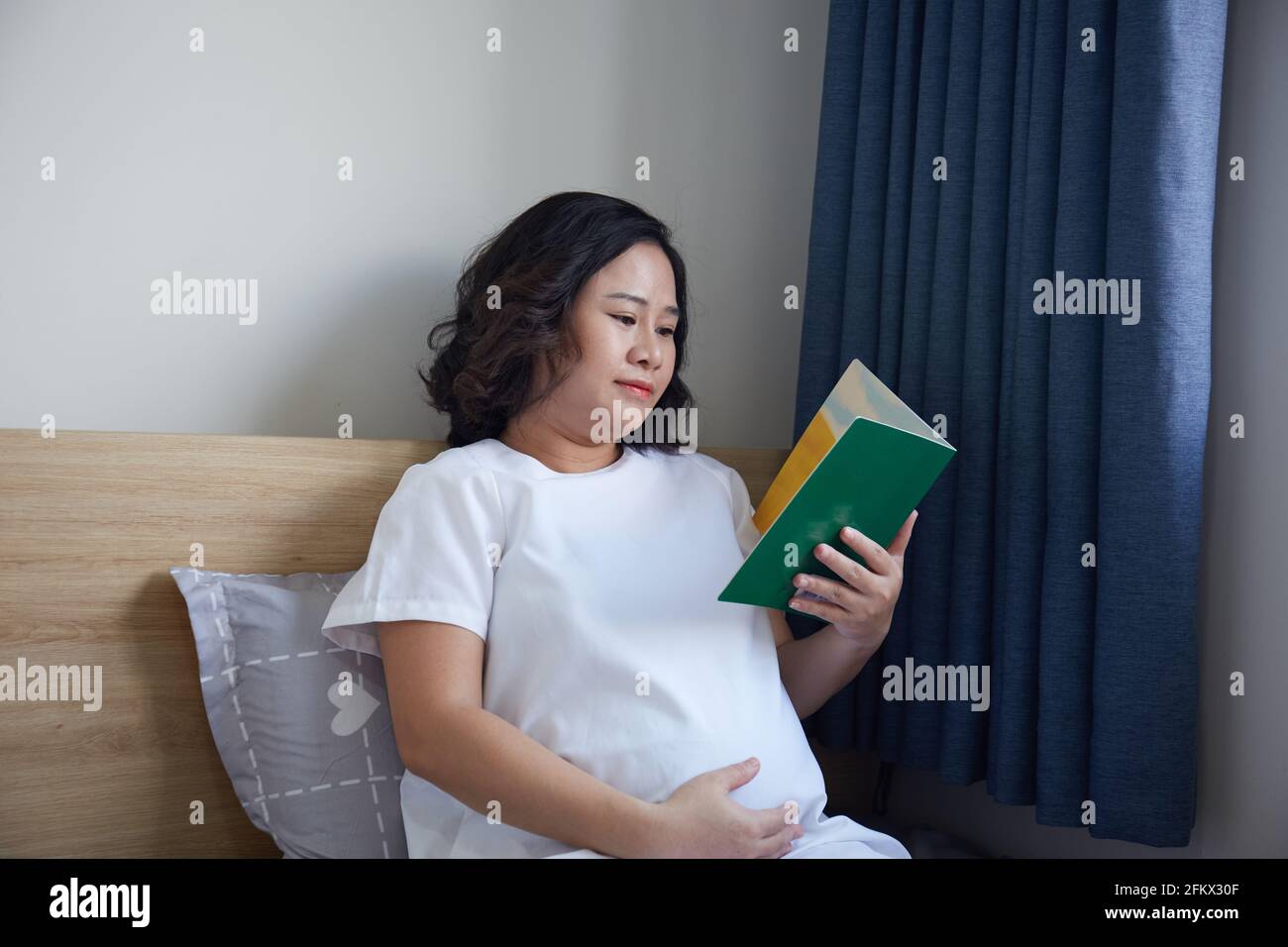 Young Vietnamese pregnant woman with short hair reading a book while