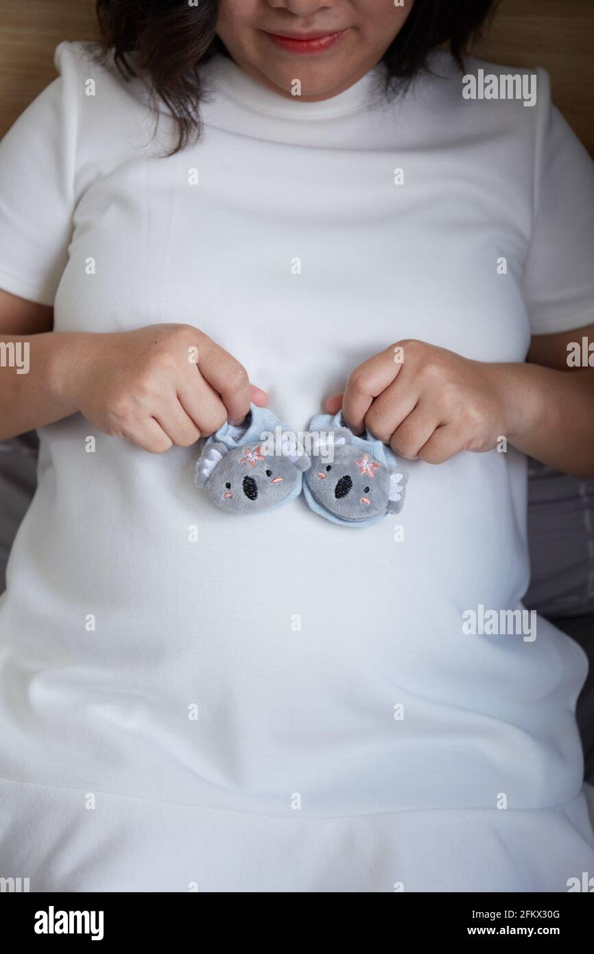 Young Vietnamese pregnant woman with short hair holding baby shoes on