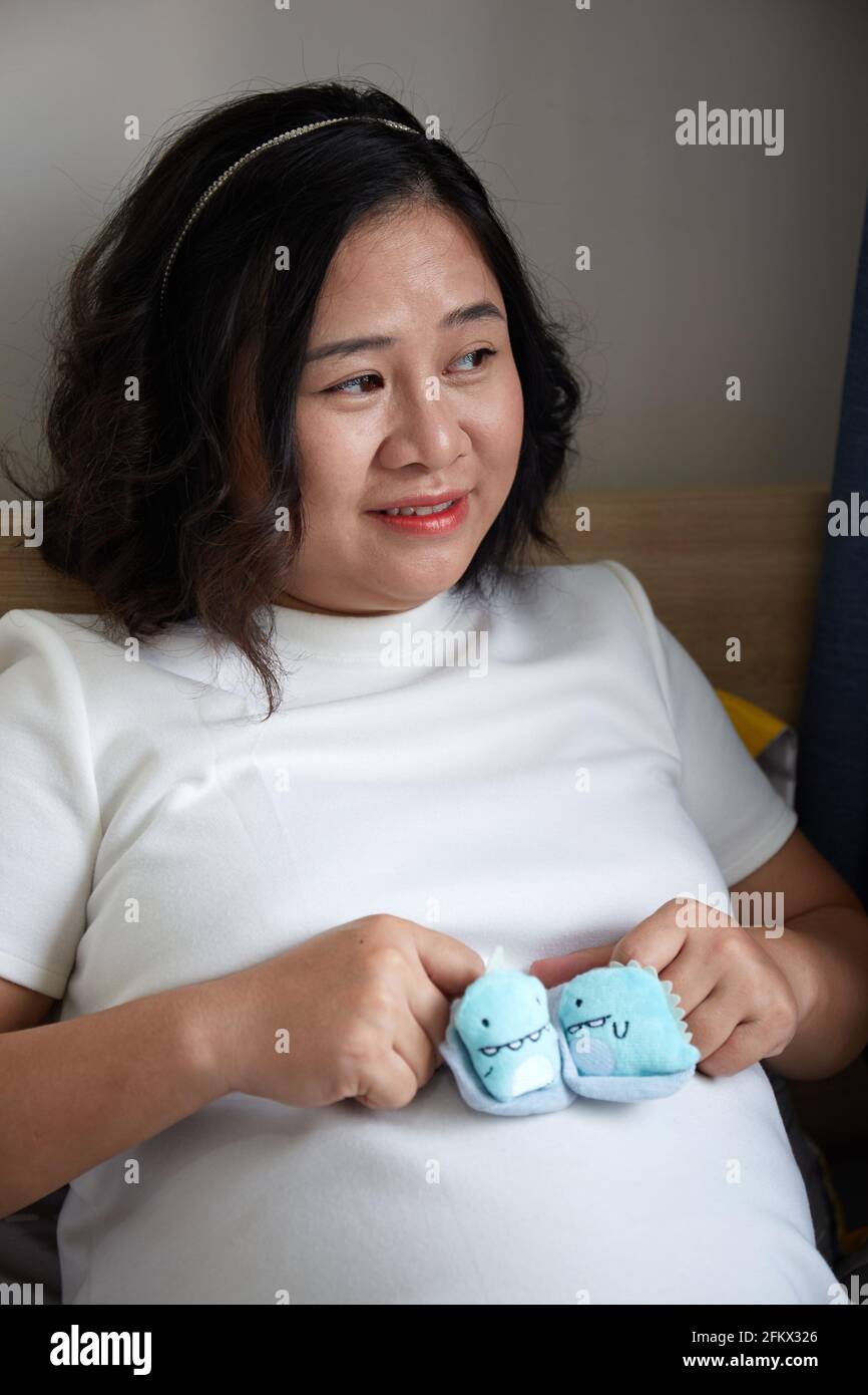 Young Vietnamese pregnant woman with short hair holding baby shoes on