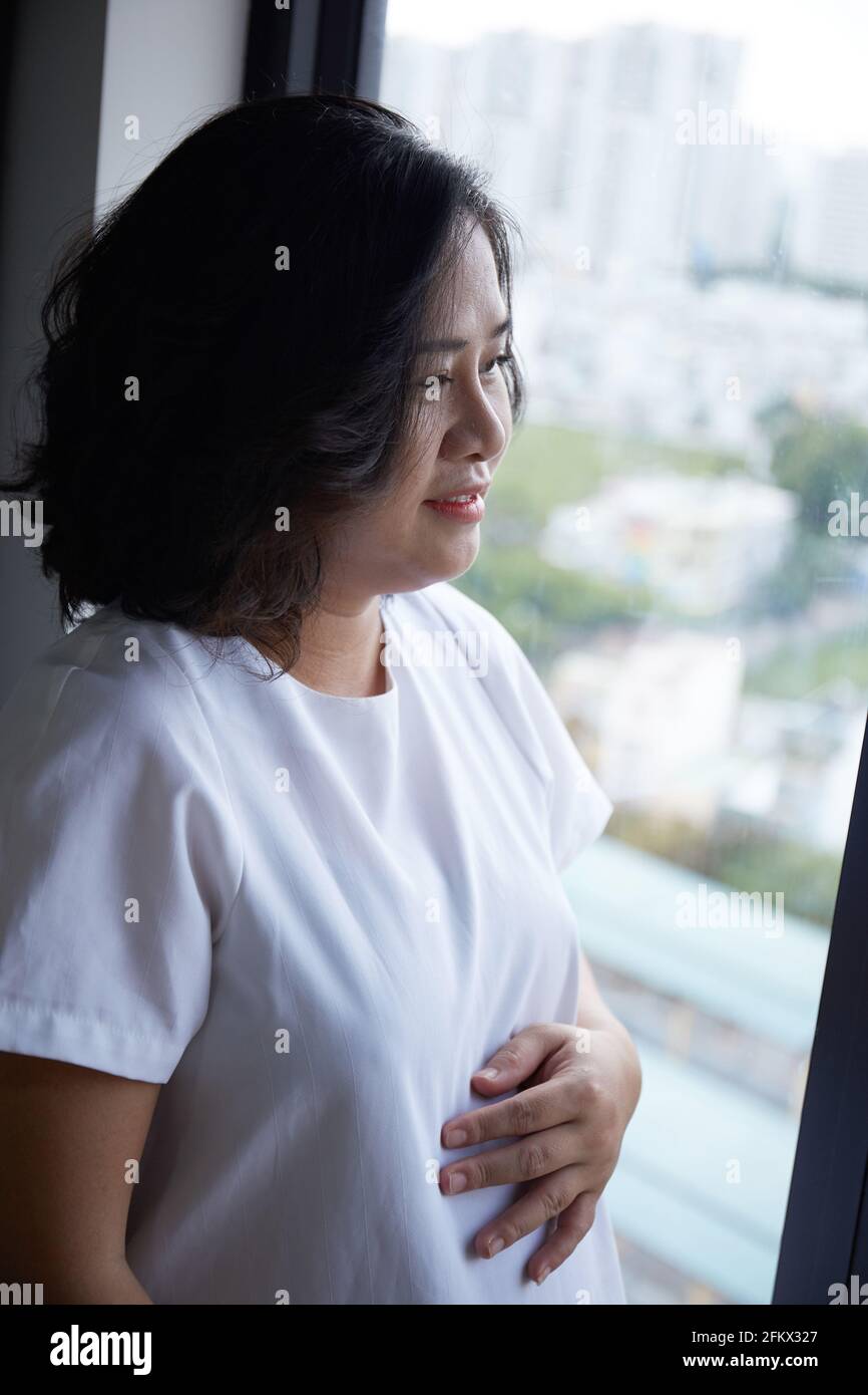 Young Vietnamese pregnant woman with short hair holding her belly while