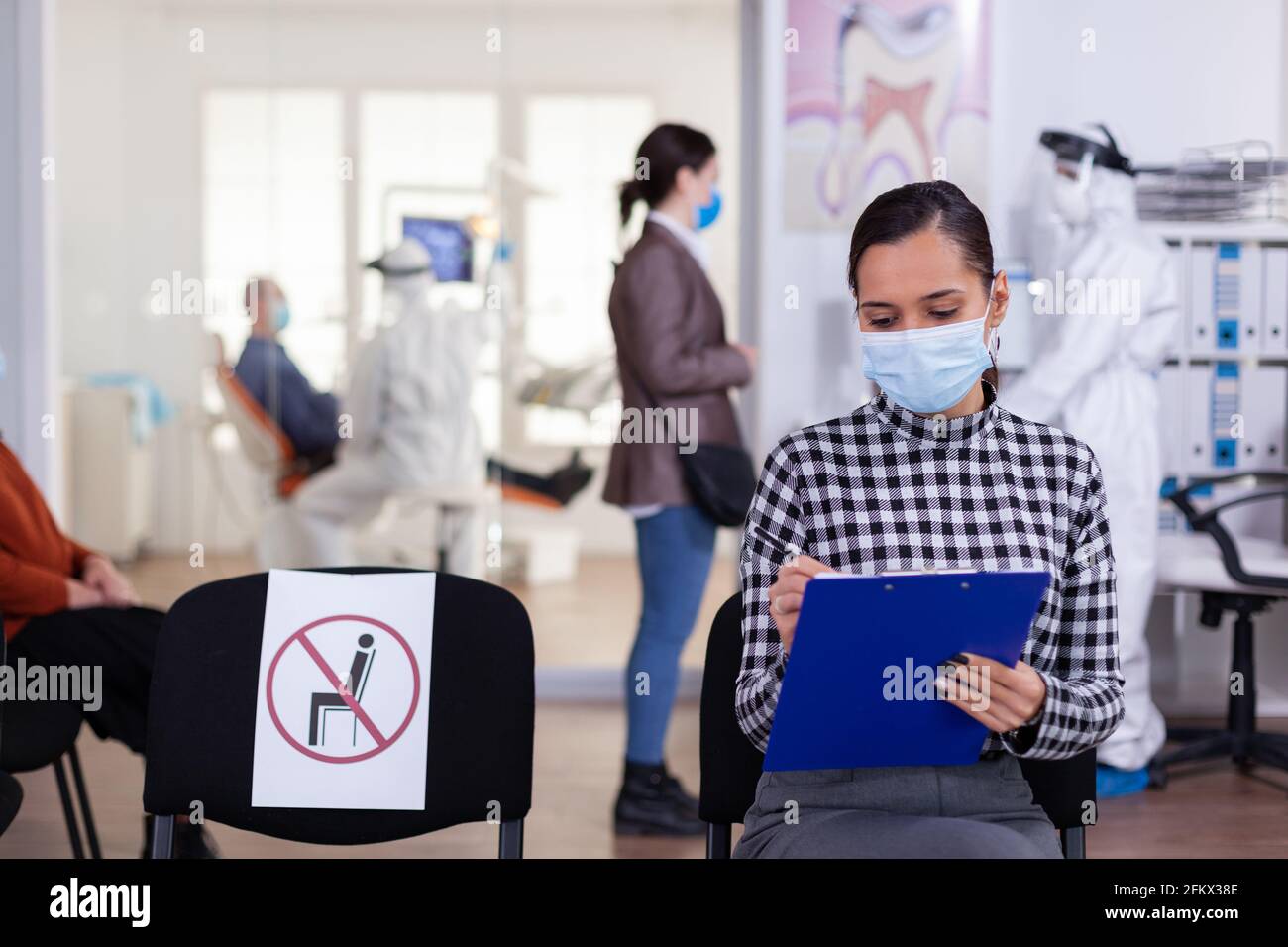 Stomatology patient in denstiry wainting area filling form before consultation with dentist dressed in ppe suit as safety precation agasint infection with coronavirus ,during global outbreak. Stock Photo