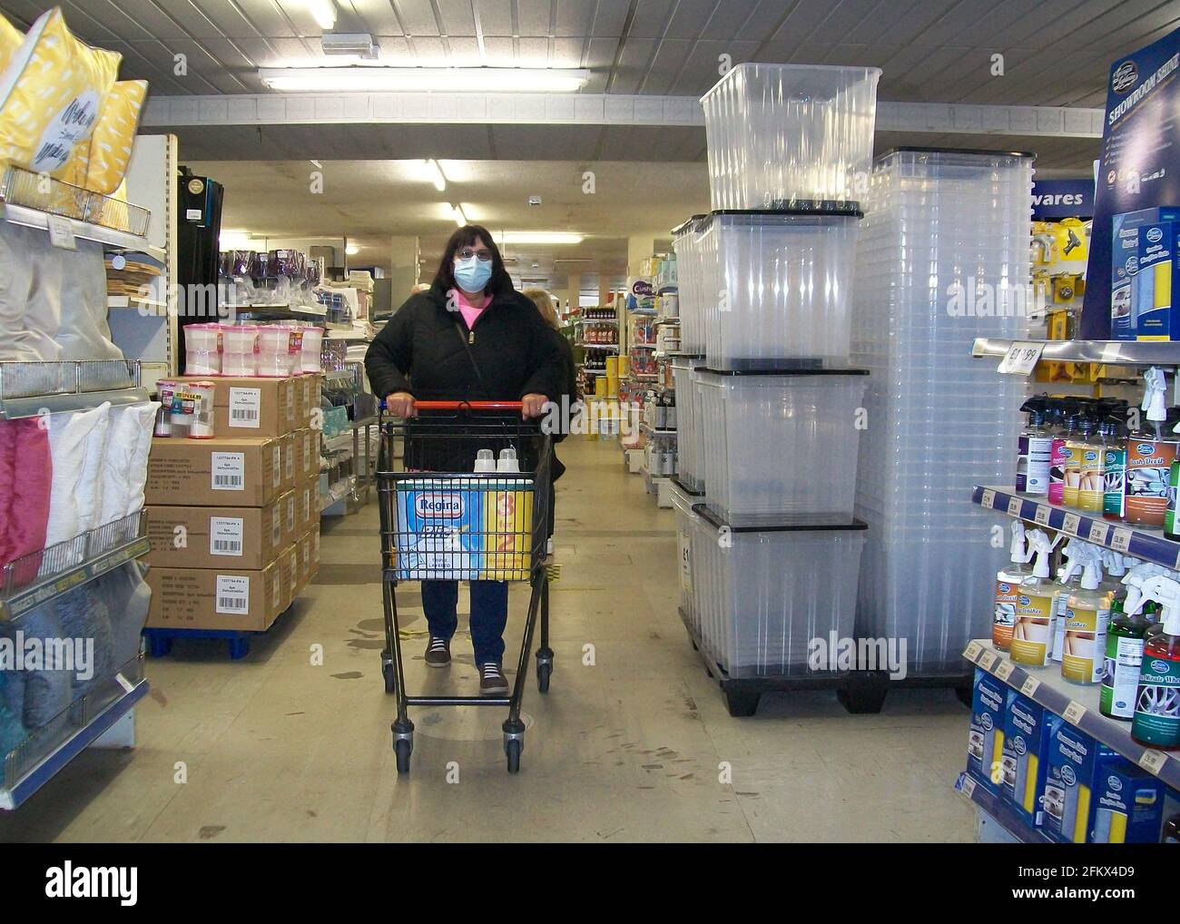 female shopper pushing shopping trolley inside supermarket wearing a face mask due to corona virus pandemic Stock Photo