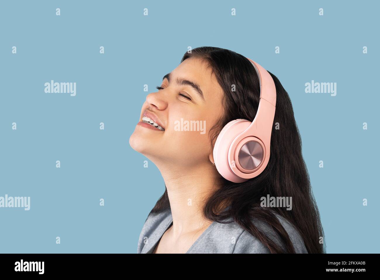 Music lover. Calm Indian teen girl in headphones listening to beautiful song with closed eyes on blue background Stock Photo
