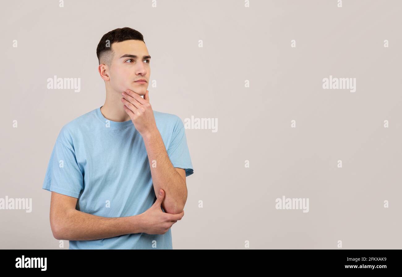 Pensive young guy thinking over problem, making decision, looking at blank space over grey studio background Stock Photo