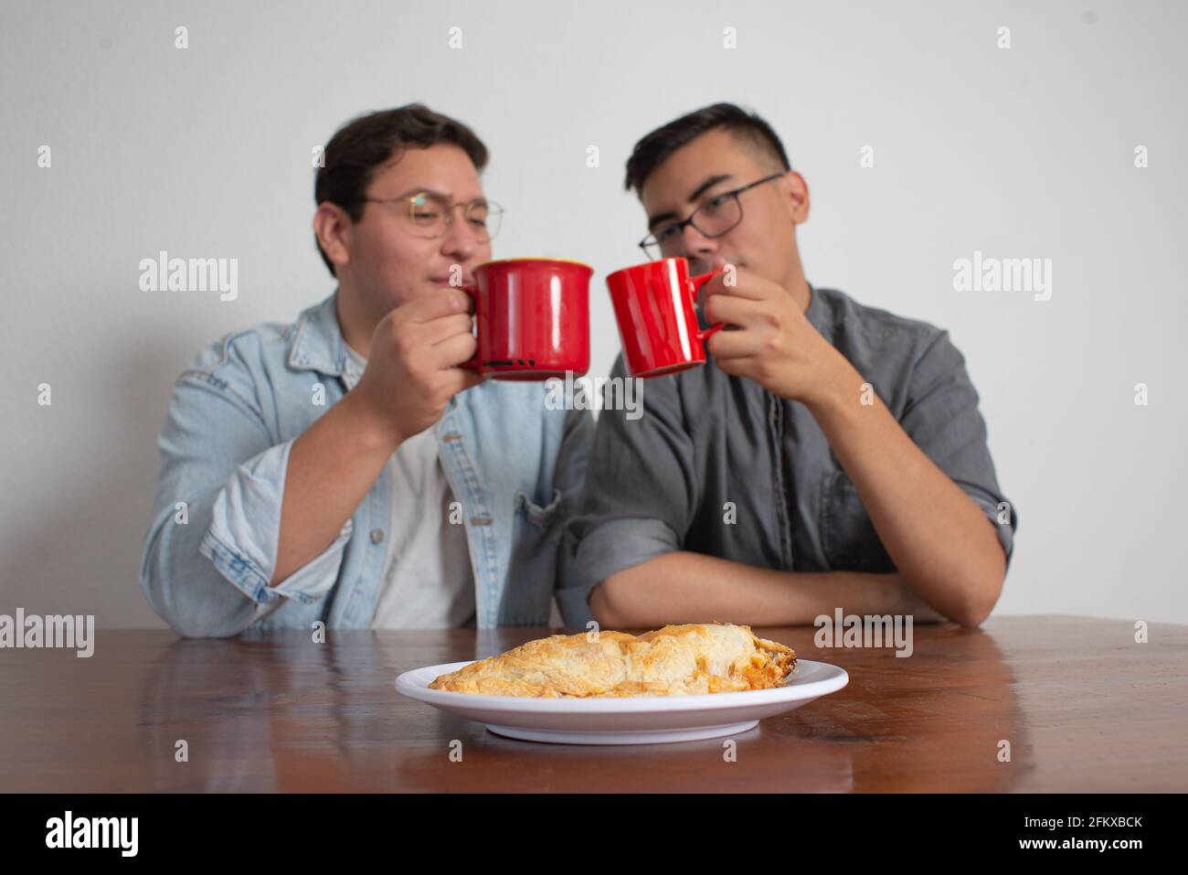 Gay Couple Having Coffee And Sharing A Molote, Delicious Mexican Dish Stock Photo