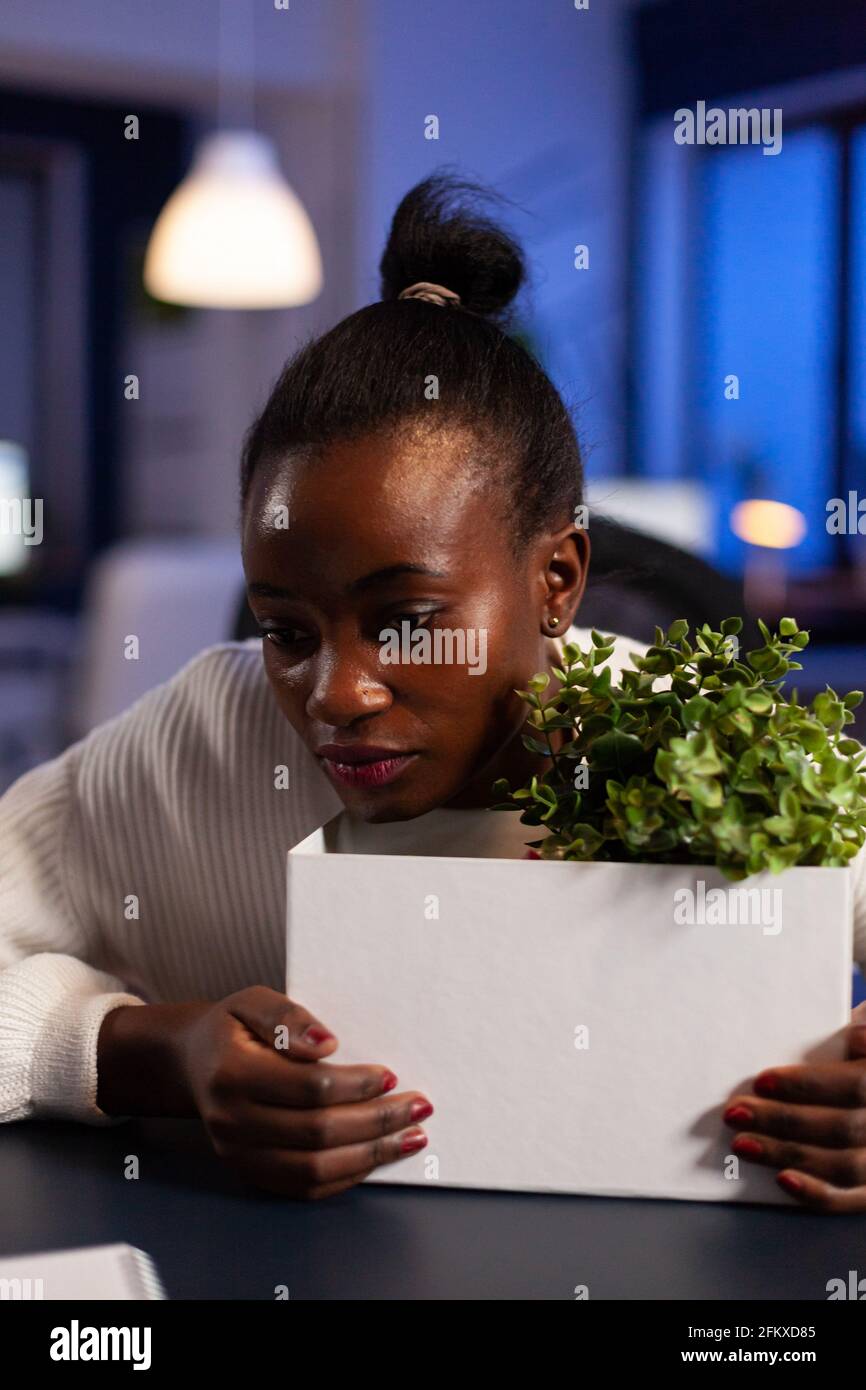 African woman depressed at night after bing let go from work because of downsizing. Unemployed packing things late at night. woman leaving workplace office in midnight. Stock Photo