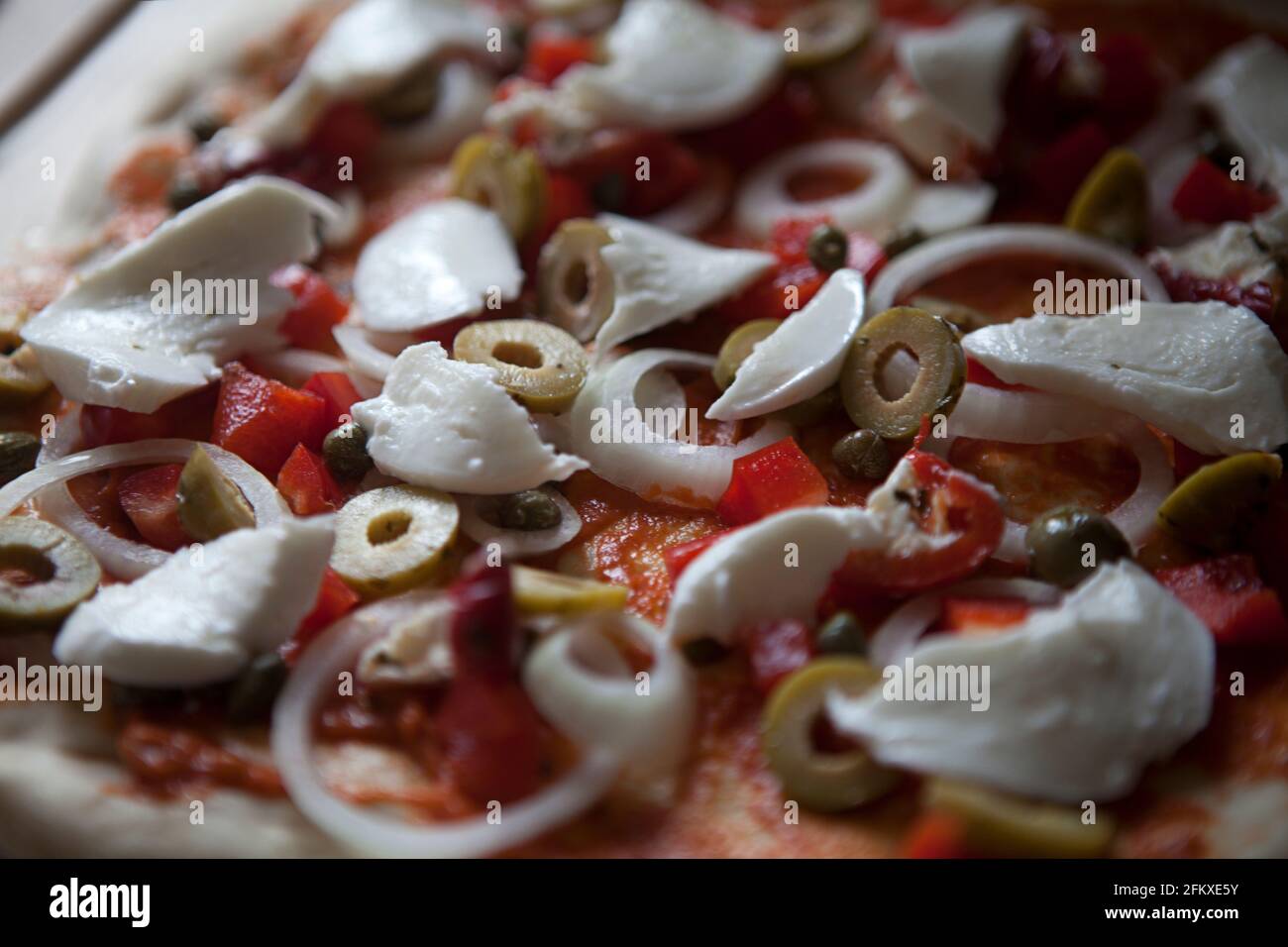 Homemade pizza before cooking, tomato base topped with red bell peppers, onions, green olives, capers and buffalo mozzarella Stock Photo