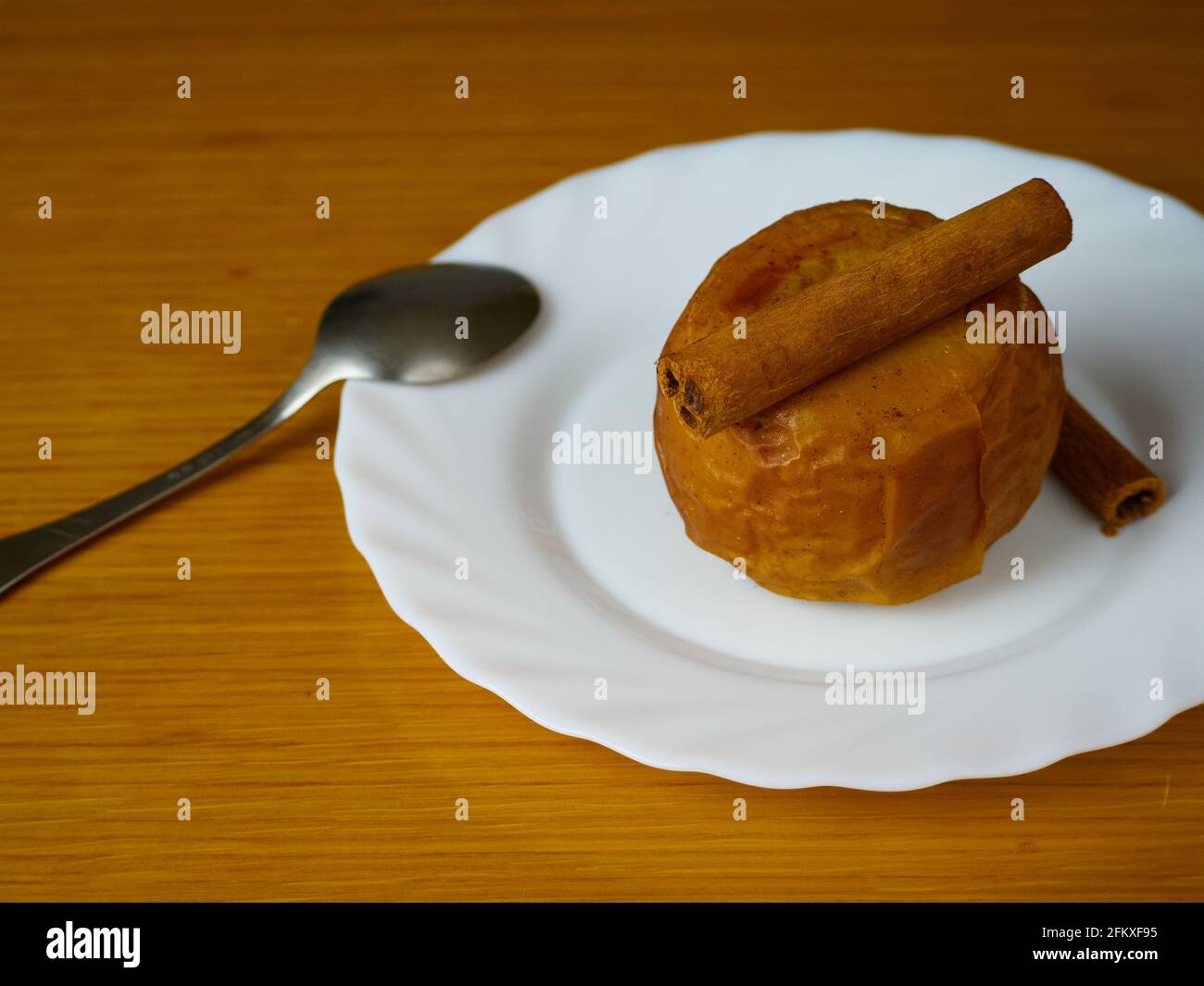 Baked Apple decorated with cinnamon sticks and a metal spoon on a plate and wooden background Stock Photo