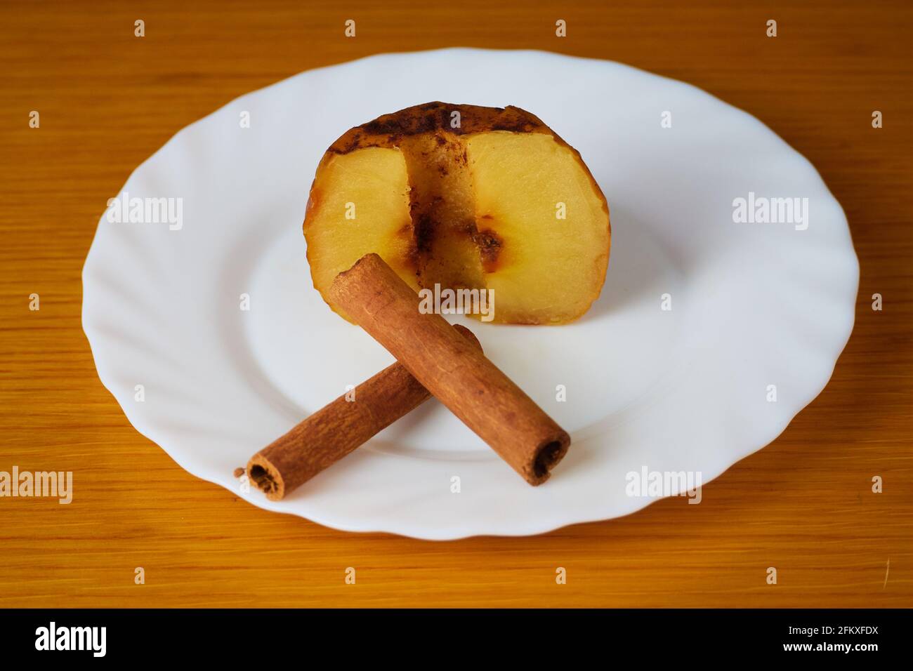 Half of Baked Apple decorated with cinnamon sticks on a plate and wooden background Stock Photo