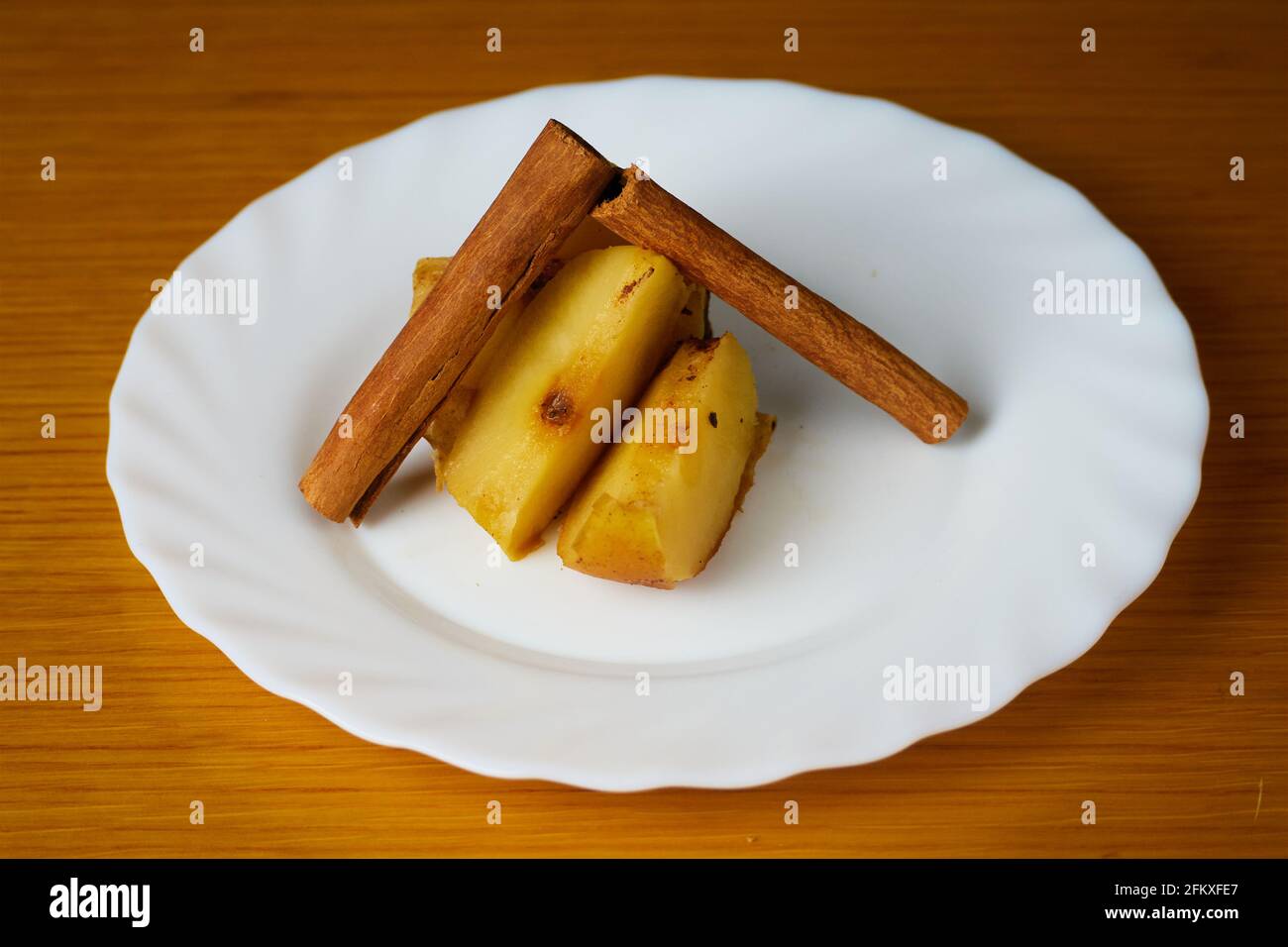 Baked Apple slices decorated with cinnamon sticks on a plate and wooden background Stock Photo