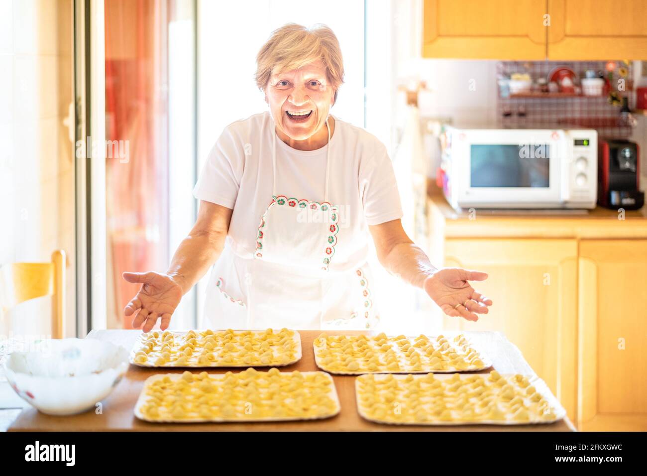 Happy woman presenting handmade ' cappelletti ' at house kitchen - Local food concept with home made italian pasta preparation - Warm bright backlight Stock Photo