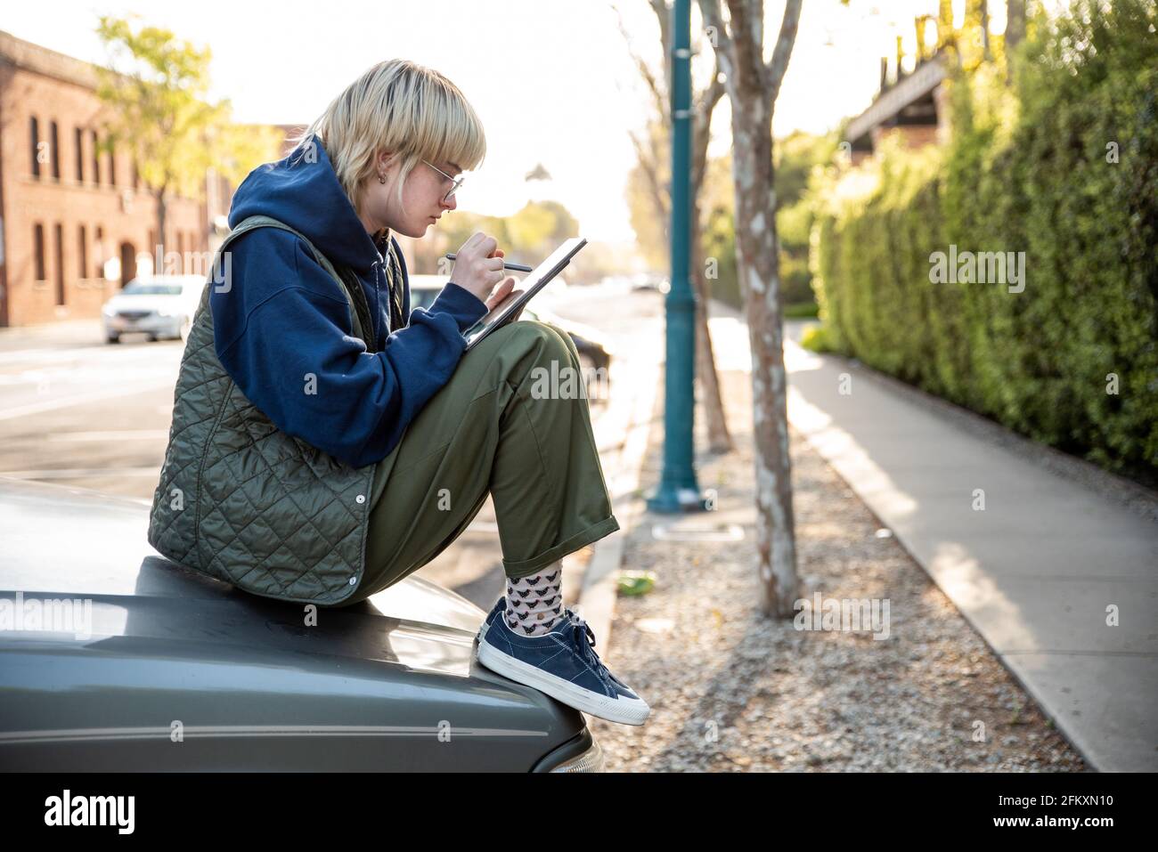 Young adult sitting on hood of truck using stylus and tablet to work Stock Photo