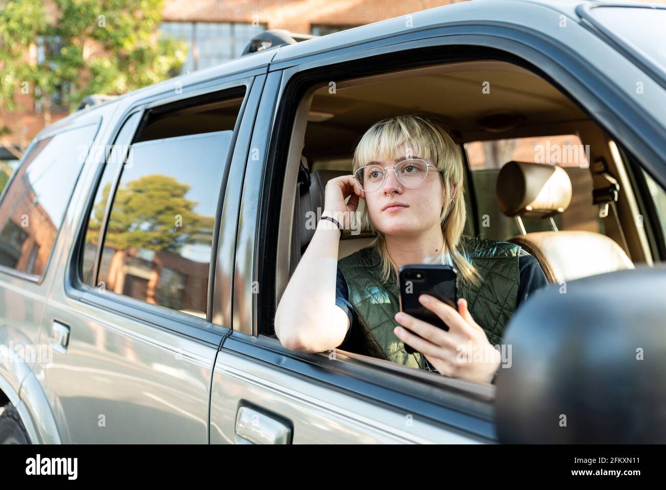 Teen looking out passenger window of car holding cel phone downtown Stock Photo