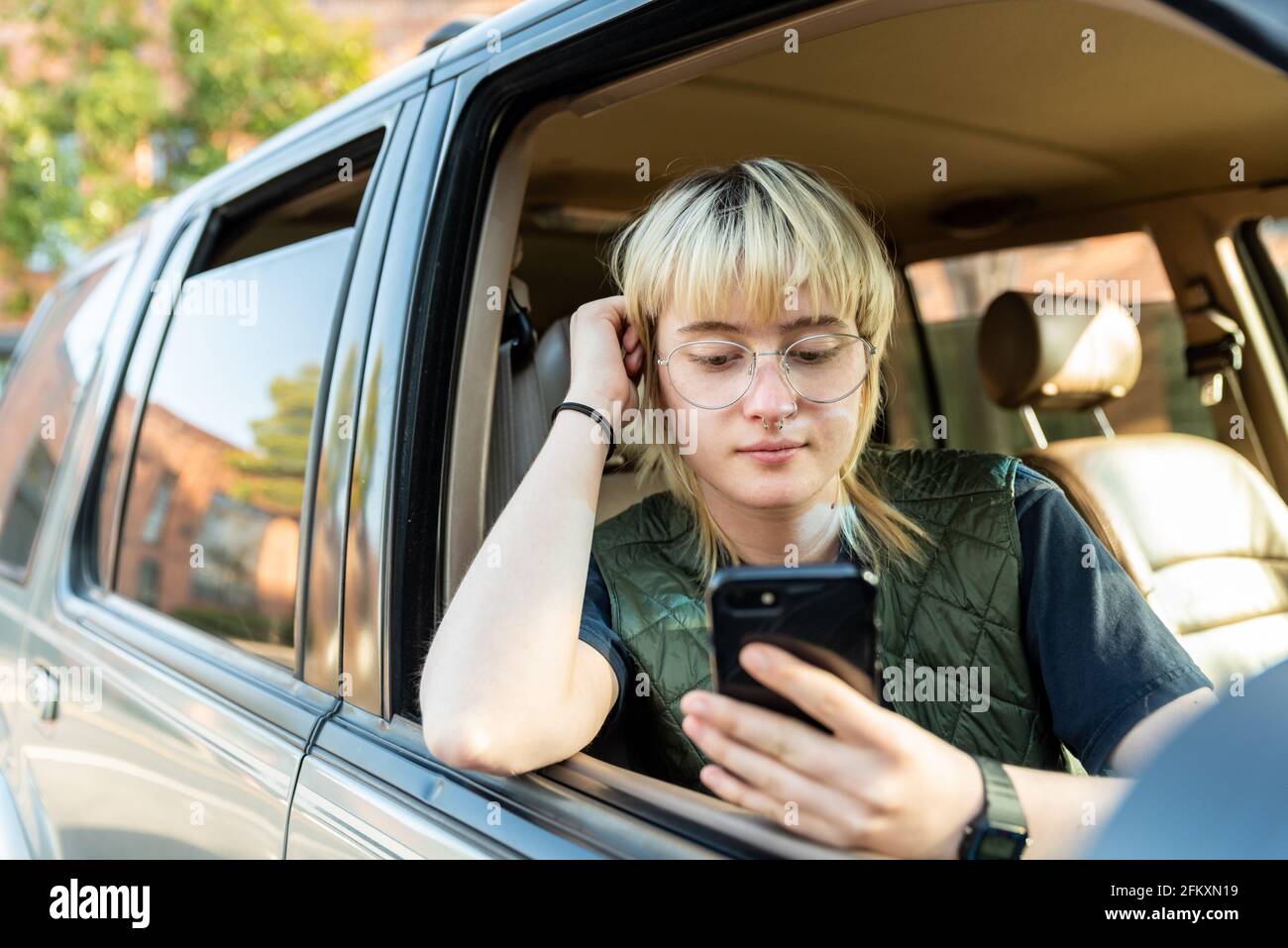 Teenager sitting in passenger seat of car looking at cell phone Stock Photo