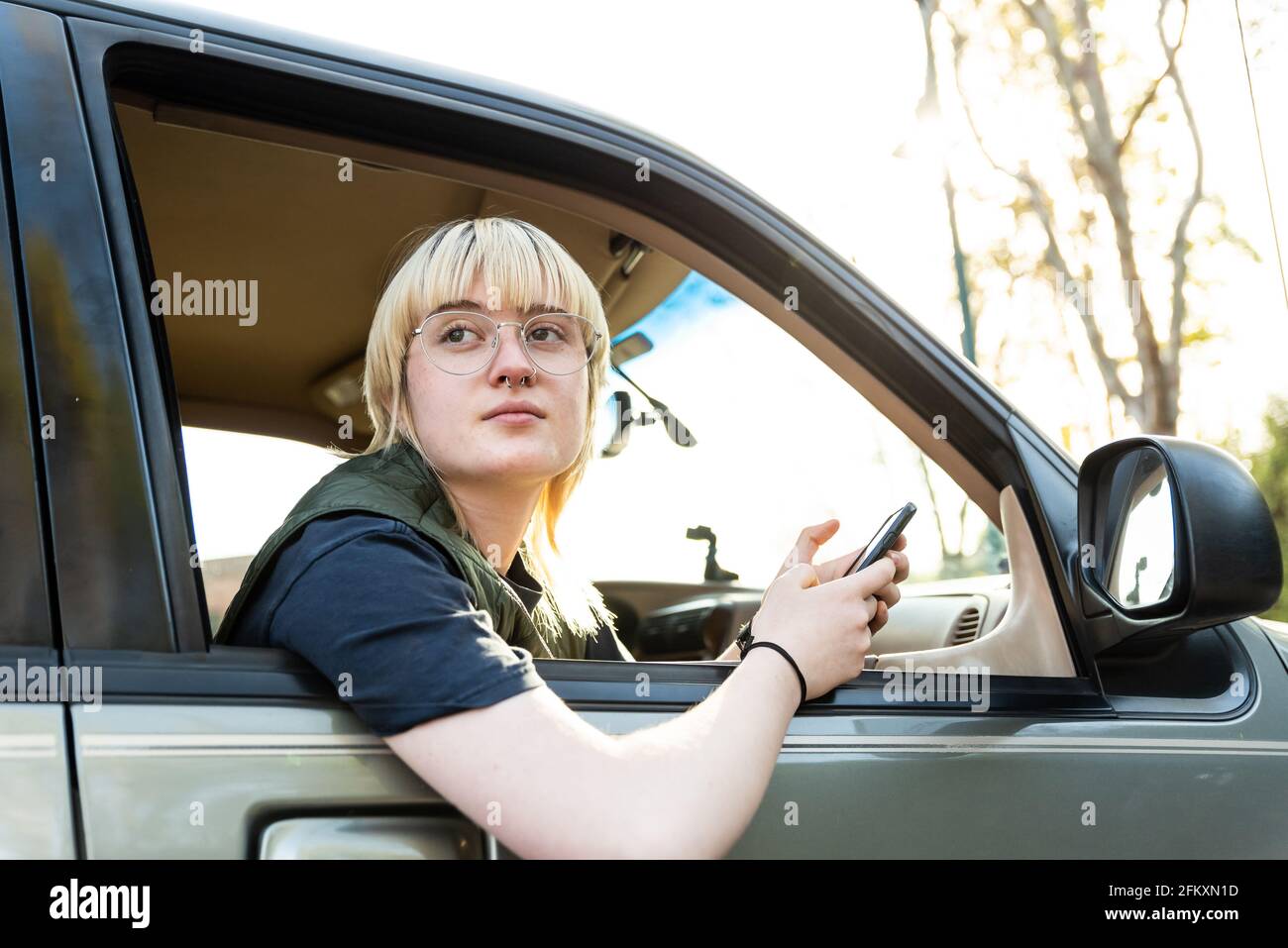 Confident teen holding cell phone leaning out passenger window of car Stock Photo