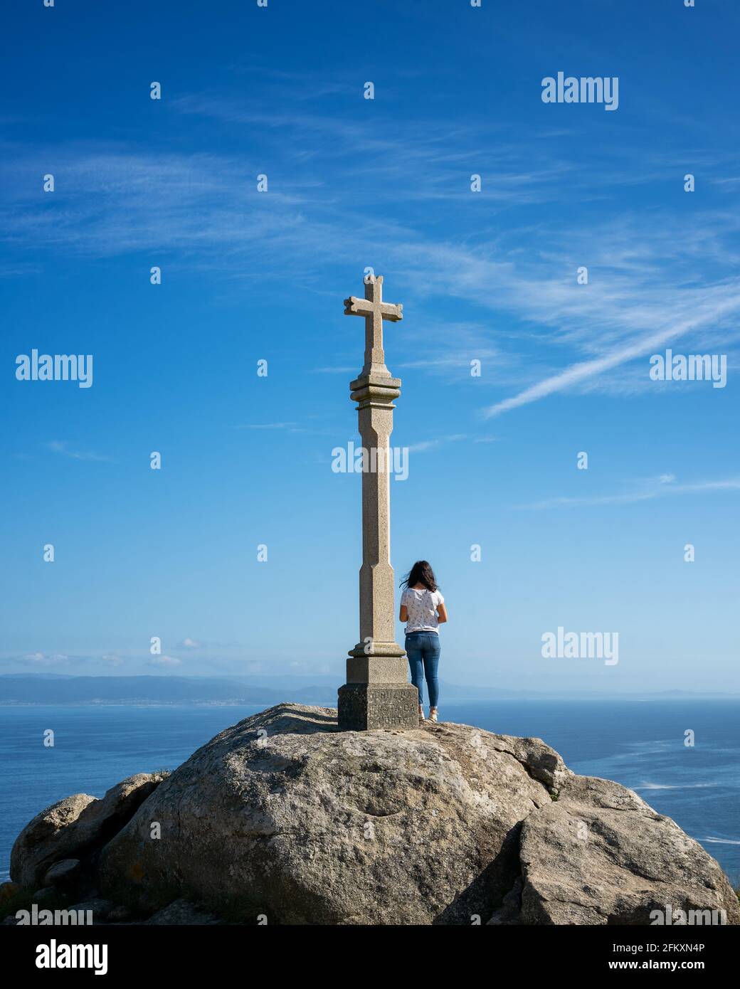 Woman on top a viewpoint rock with a cross sculpture in Finisterre Stock Photo