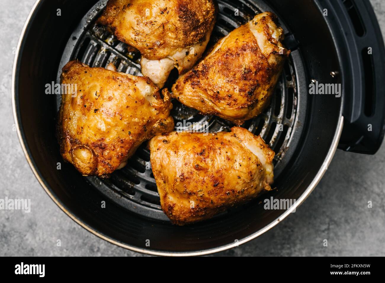 Four spicy air fried chicken thighs in an air fryer Stock Photo