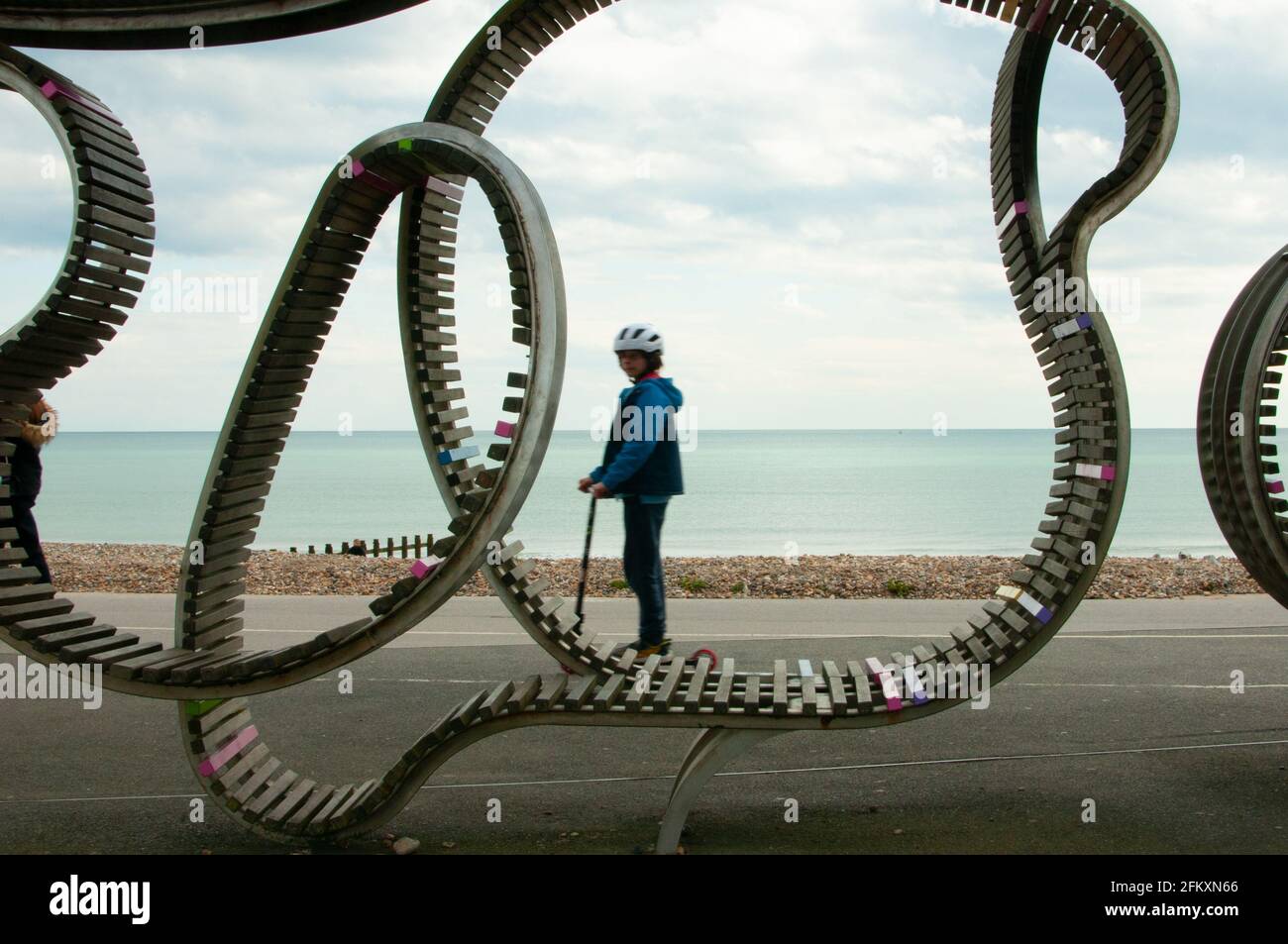 boy on scooter on Littlehampton Promenade by long bench, West Sussex UK Stock Photo