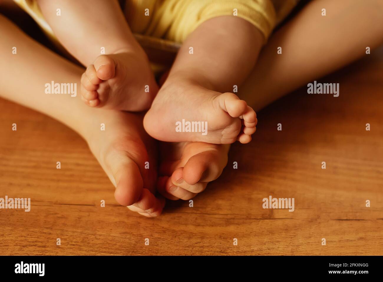 Two girls sisters different age sit together barefoot on wooden floor Stock Photo