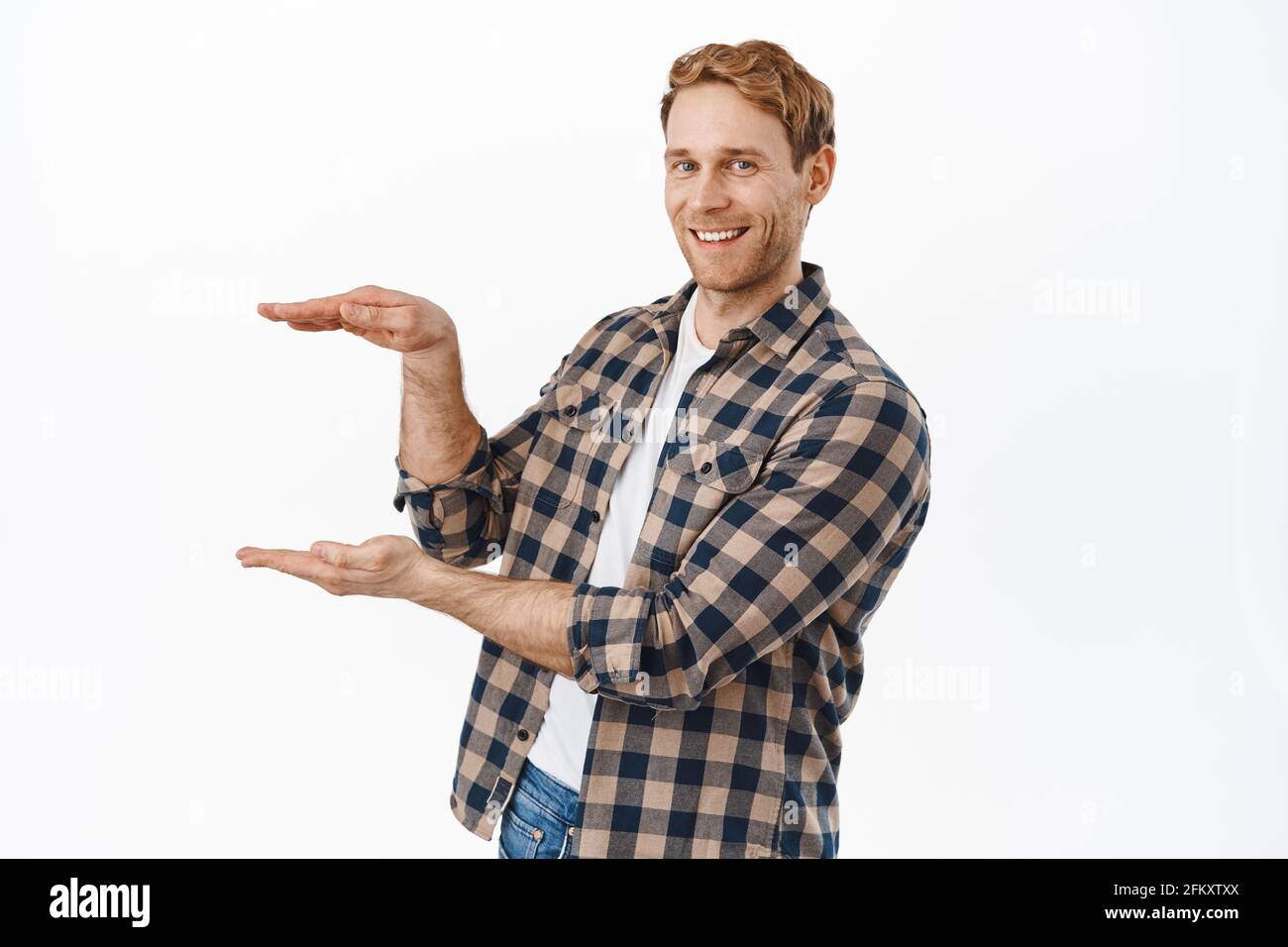 Image of strong and handsome redhead man holding your product logo against white copyspace, making empty box gesture and smiling at camera, display Stock Photo