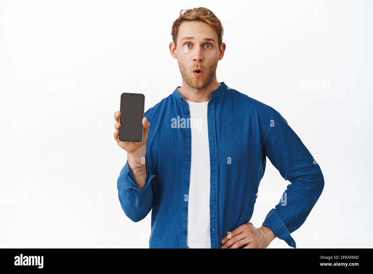 Surprised redhead man showing application on smartphone screen. Guy shows mobile phone display