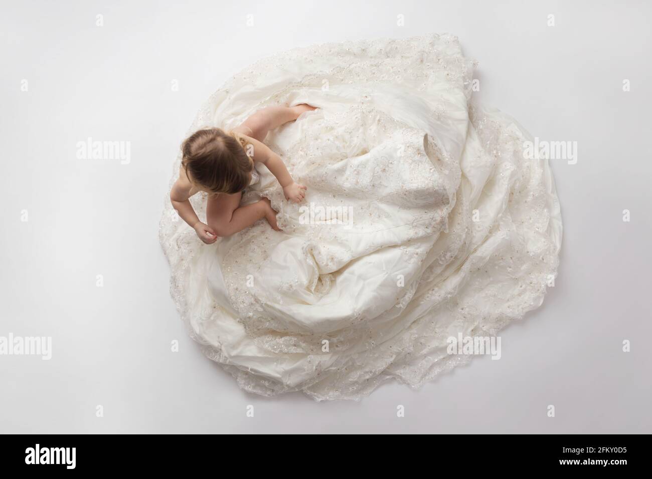 Toddler girl looks at bodice of mother's wedding gown Stock Photo