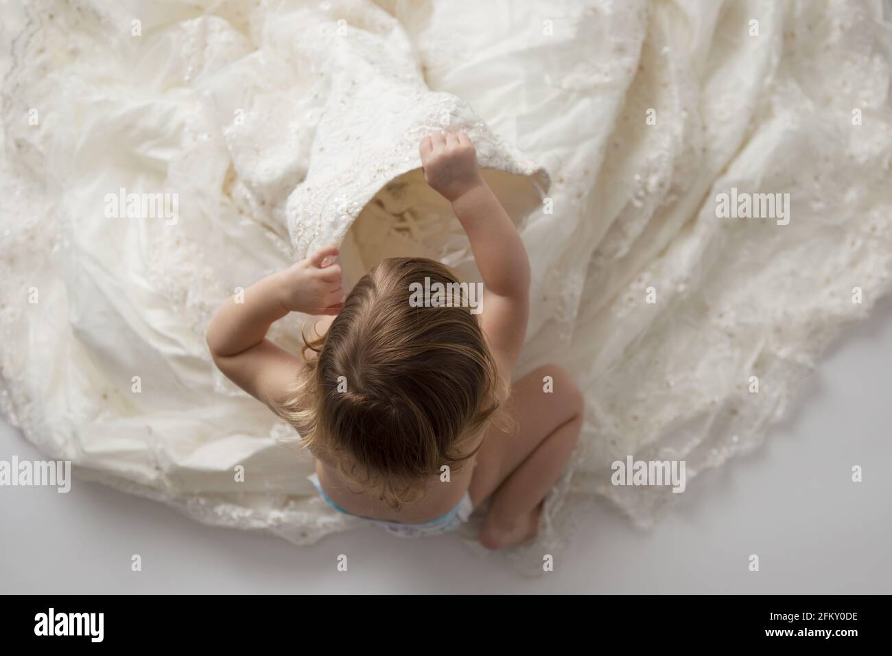 Toddler girl looks inside bodice of mother's wedding gown Stock Photo