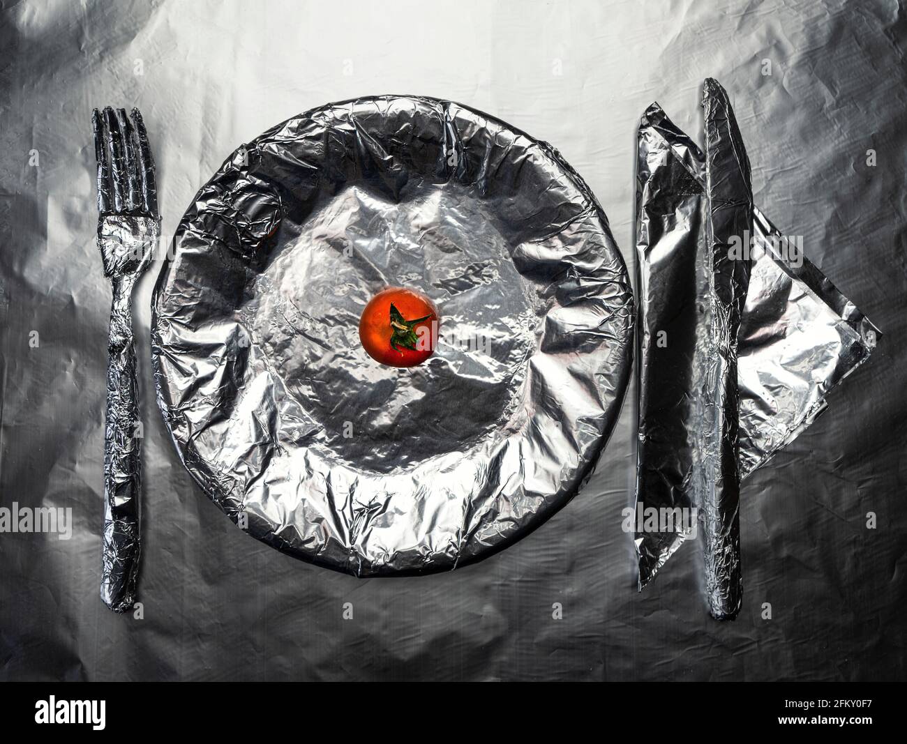 home plate, crockery and a glass covered with aluminum foil with a small tomato Stock Photo