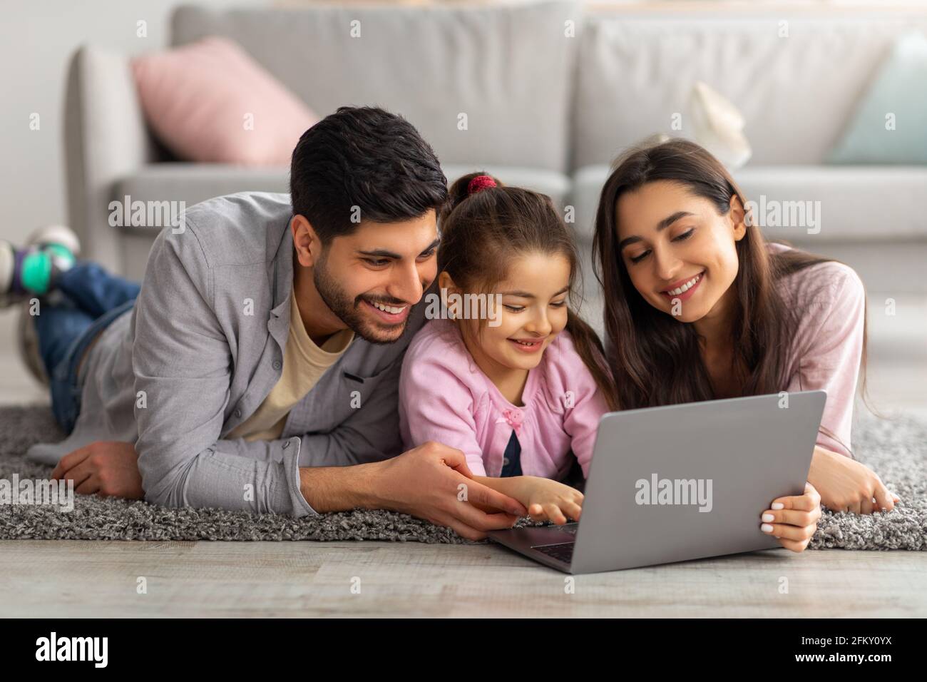 Family weekend. Cheerful arab parents teaching their little daughter using laptop, spending time at home together Stock Photo