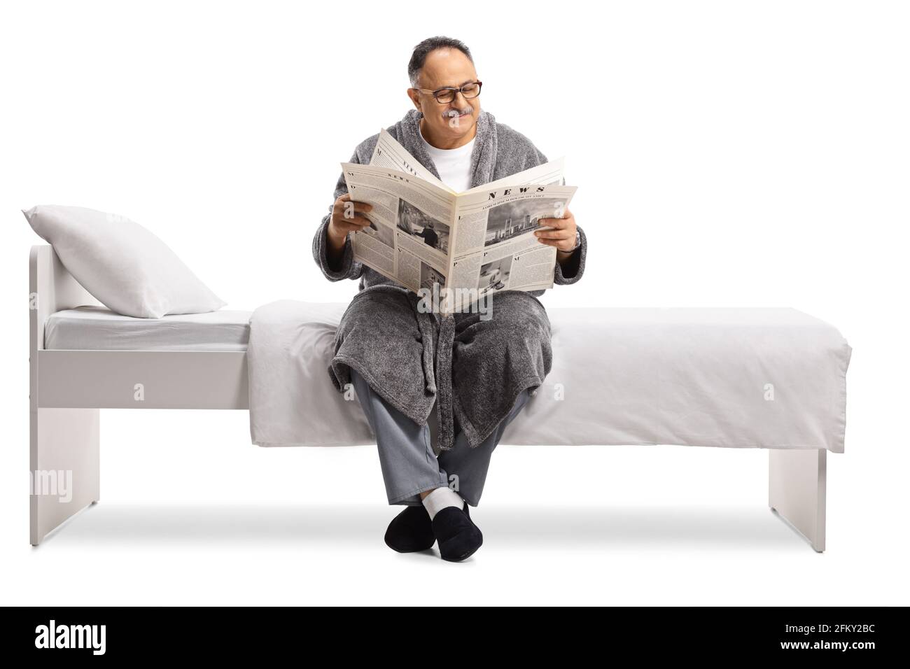 Mature man in a robe relaxing on a bed with a newspaper isolated on white background Stock Photo