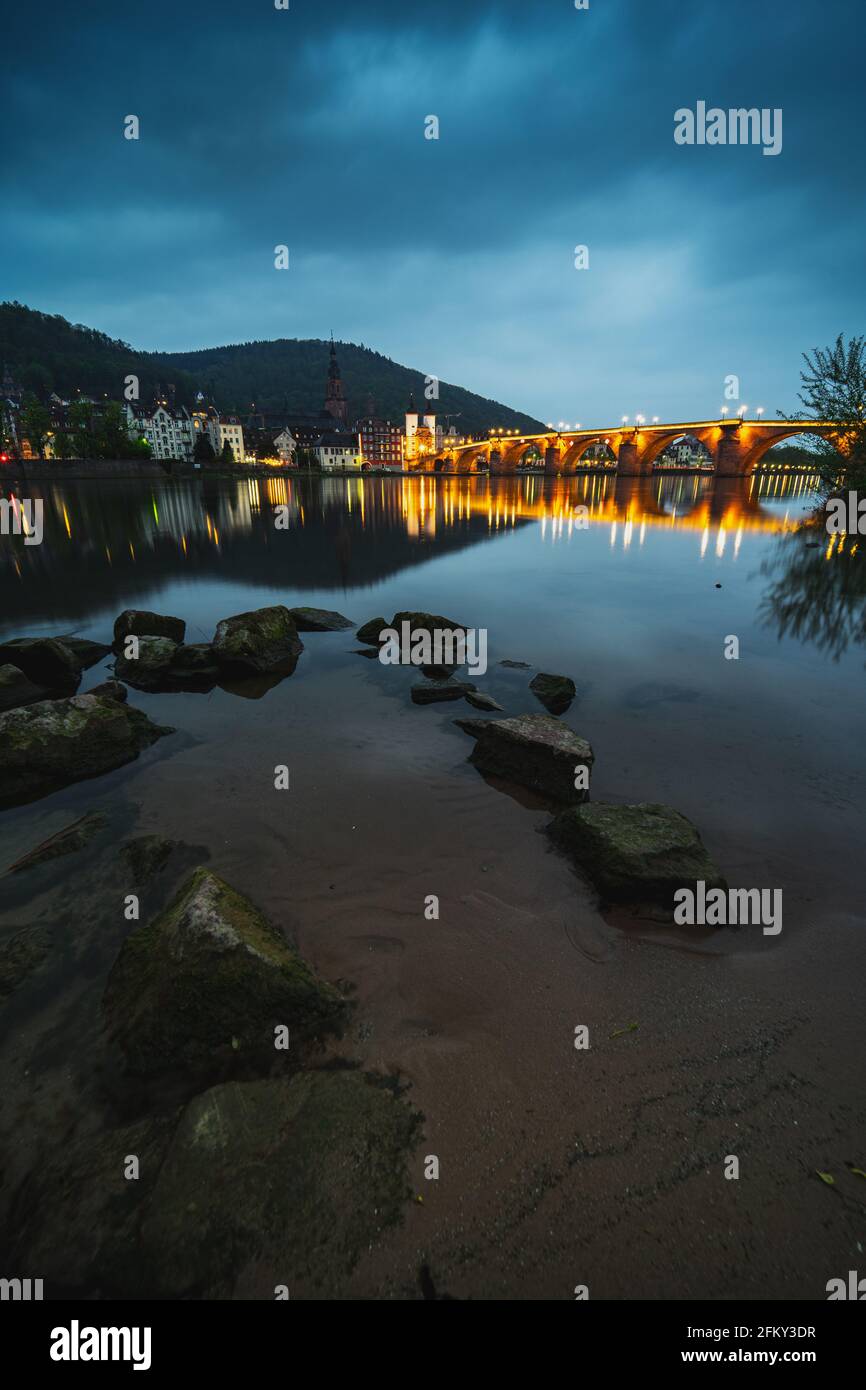Beautiful sunset of the old bridge in Heidelberg. The illumination of the old bridge reflects in the calm water. Stock Photo