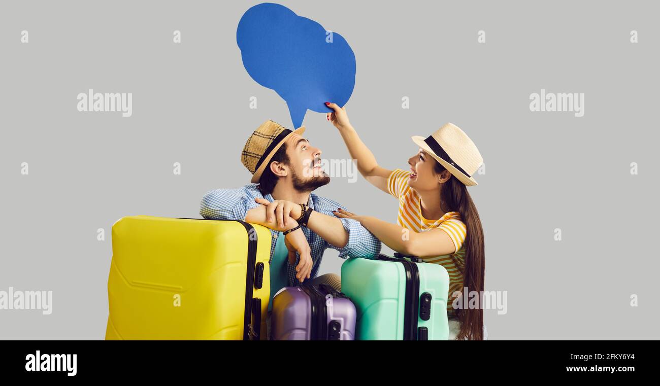Couple of happy young tourists with suitcases holding speech balloon or thought bubble Stock Photo