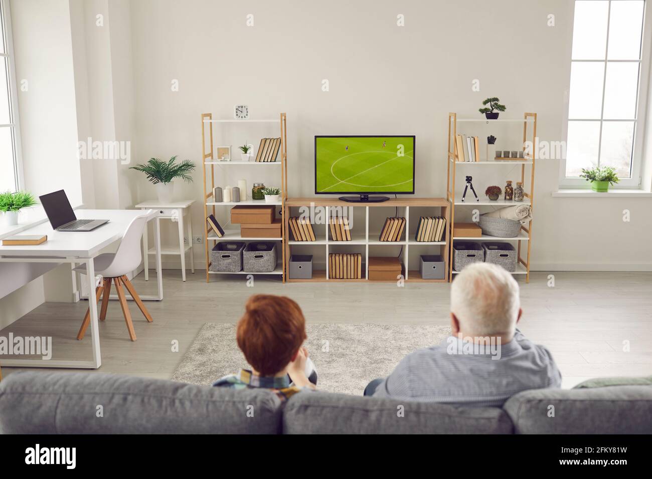 Back view of grandpa and grandson sitting on sofa and watching football match on TV Stock Photo