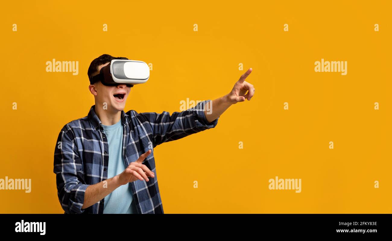 Cool young guy in virtual reality headset controlling cyber environment, pushing invisible button on virtual screen Stock Photo