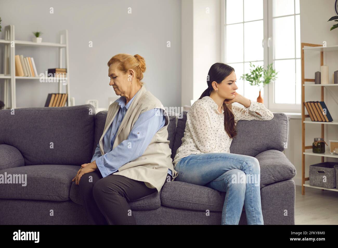 Offended older woman and her adult daughter are sitting on the couch with their backs to each other. Stock Photo