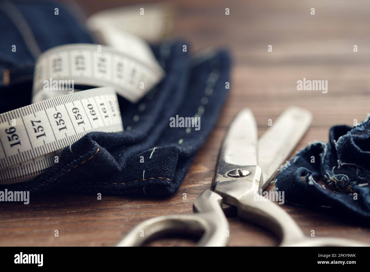 Shortening jeans. Measuring tape and tailoring scissors on table. Jeans cutting. Stock Photo